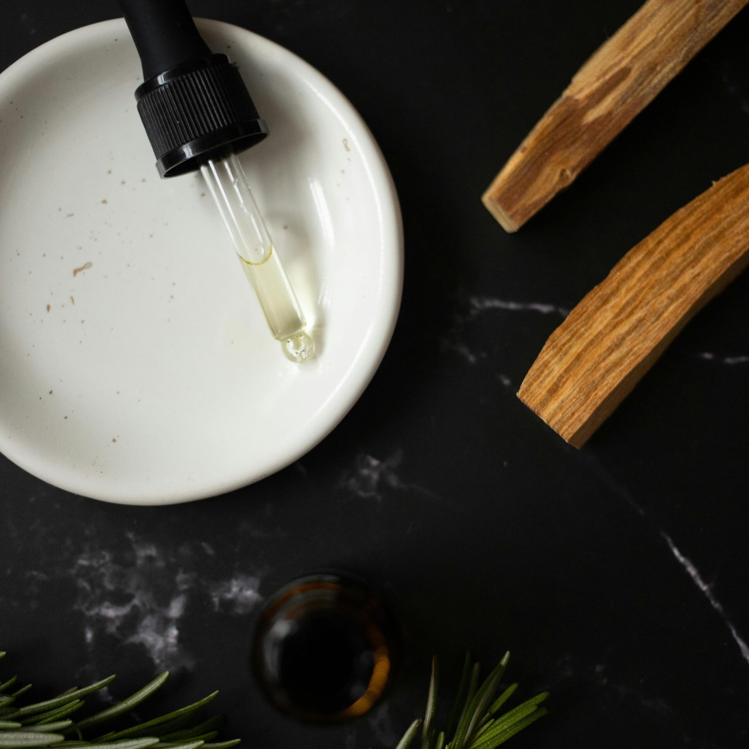 Top view of white clean plate with aromatic oil composed with timber sticks and fresh verdant branches of rosemary